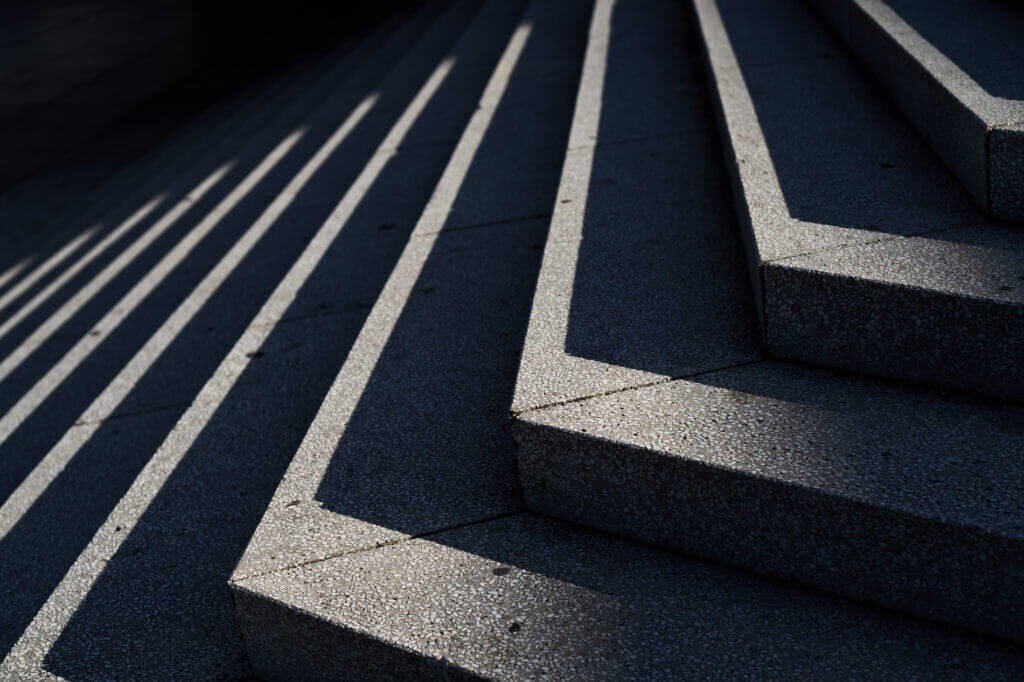 die schräg stehende Sonne zeichnet Schatten auf Stufen, die die Treppe schmaler und empfidlicher erscheinen lässt, als der Beton aus kleinen Kieseln am Tag erscheint.